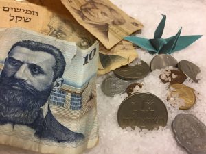 ברבור אוריגמי ירוק שמסמל רכות לצד יצירתיות ודיוק, מונח בין שטרות ומטבעות ישראלים מתקופות עבר. להמחשת המסר שביופי שקיים במכירות ערכיות.